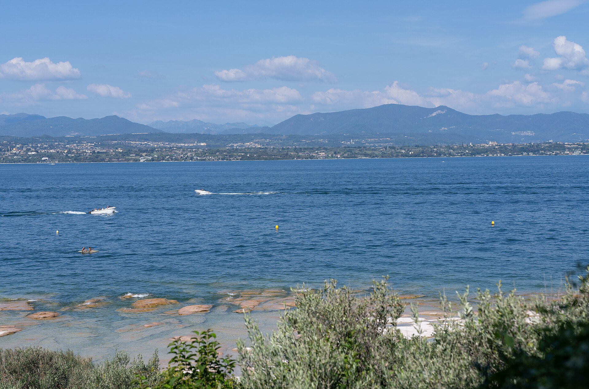 View from Sirmione, Italy, across Lake Garda towards the opposite shore and mountains. Motorboats cross the la