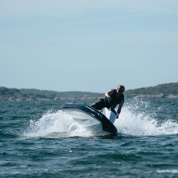 A rider leaning into a turn on a ROXEN electric watercraft, spray flying, off a rocky coastline